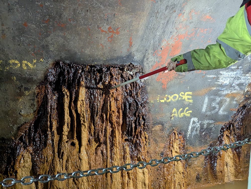 A tunnel engineer prods the soft iron ore deposits seeping out of Harecastle Tunnel to test the underlying concrete repair.